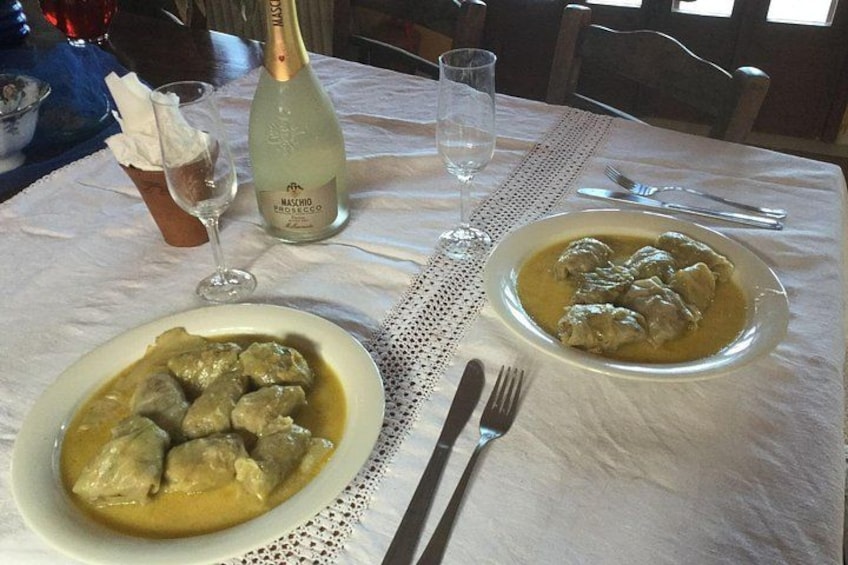 Une table avec une bouteille de vin Maschio di Modena, deux verres, une assiette de boulettes de viande à la sauce et une serviette pliée. 5