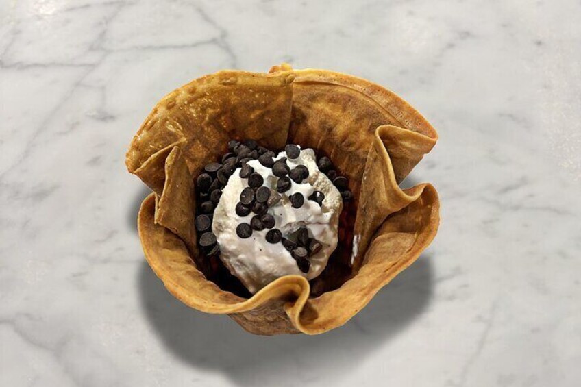 A dessert in a waffle bowl with chocolate chips and whipped cream. 3