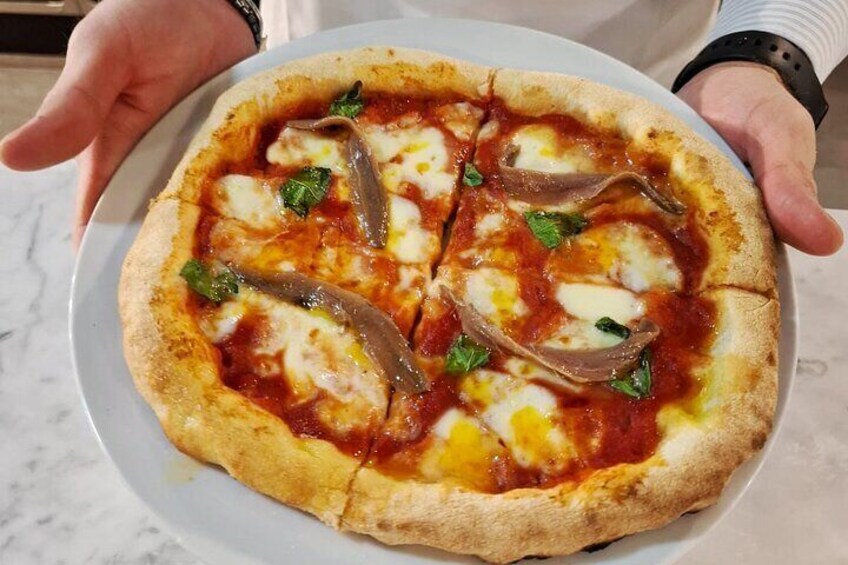 A pizza with cheese, anchovies, and basil on a white plate. 1