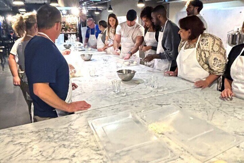 A group of people engaged in a cooking class around a marble countertop with cooking utensils and ingredients. 2