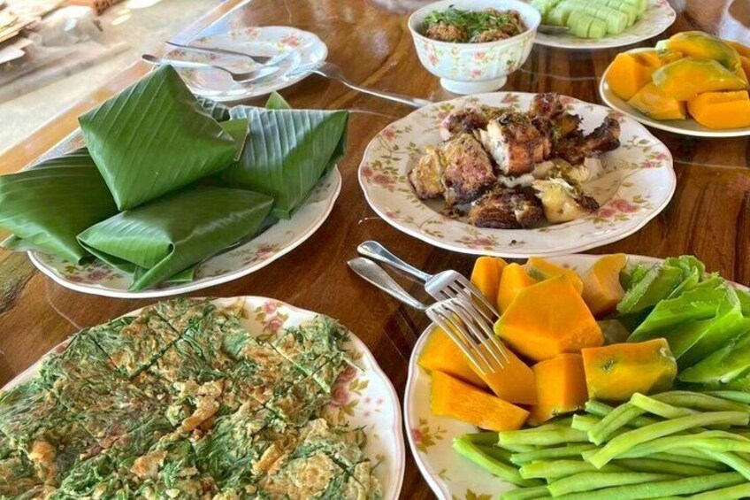 A variety of dishes including banana leaves, grilled meat, and vegetables on a wooden table. 2