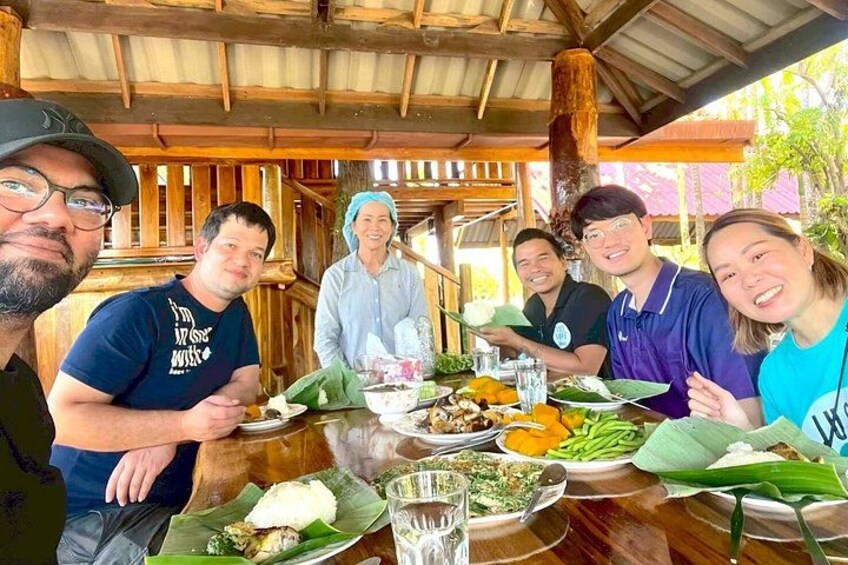 A group of people dining at an outdoor wooden table with various dishes and drinks. 3