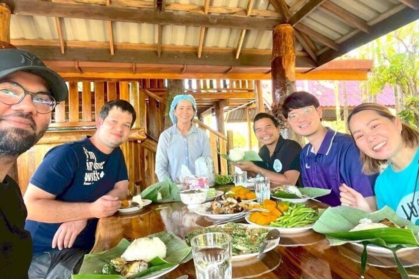A group of people dining at an outdoor wooden table with various dishes and drinks. 3
