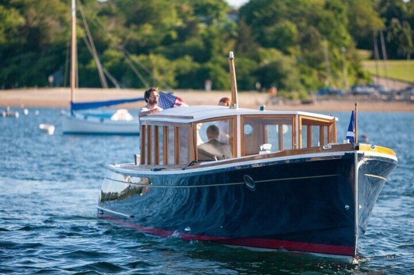 A small boat with a cabin on the water, surrounded by other boats and a shoreline with trees. 5