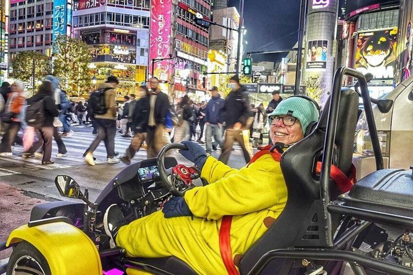 A person in a yellow outfit driving a yellow vehicle on a busy street with pedestrians and buildings in the background. 2
