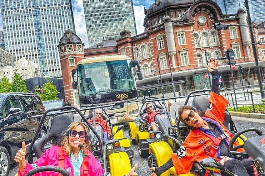 People in yellow and orange vehicles on a road with a bus and a historic building in the background. 4