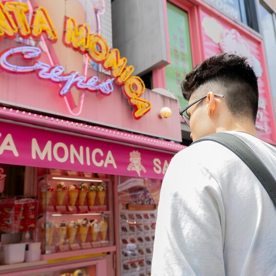 A person standing in front of a brightly lit ice cream shop with a neon sign that reads 'MONICA Crepes.' 2