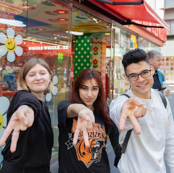 Three people pointing at a colorful storefront with a flower pattern and a sign that reads 'WIGGLE WIGGLE.' 4