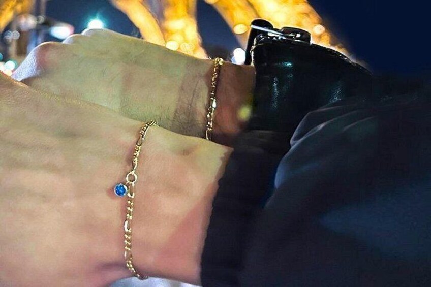 En närbild på händer som bär armband, varav ett har en blå sten, och en kamera. 1