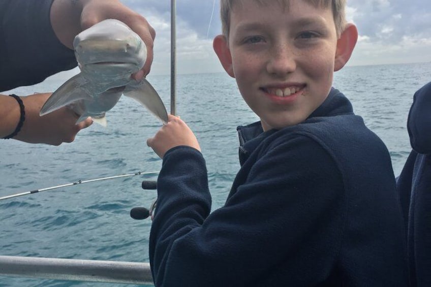 Eine Person hält einen Fisch in einem Boot, im Hintergrund das Meer. 3