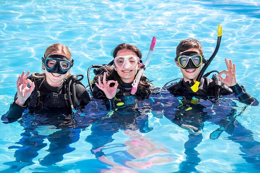 Three people in a swimming pool wearing scuba gear and making hand gestures. 2