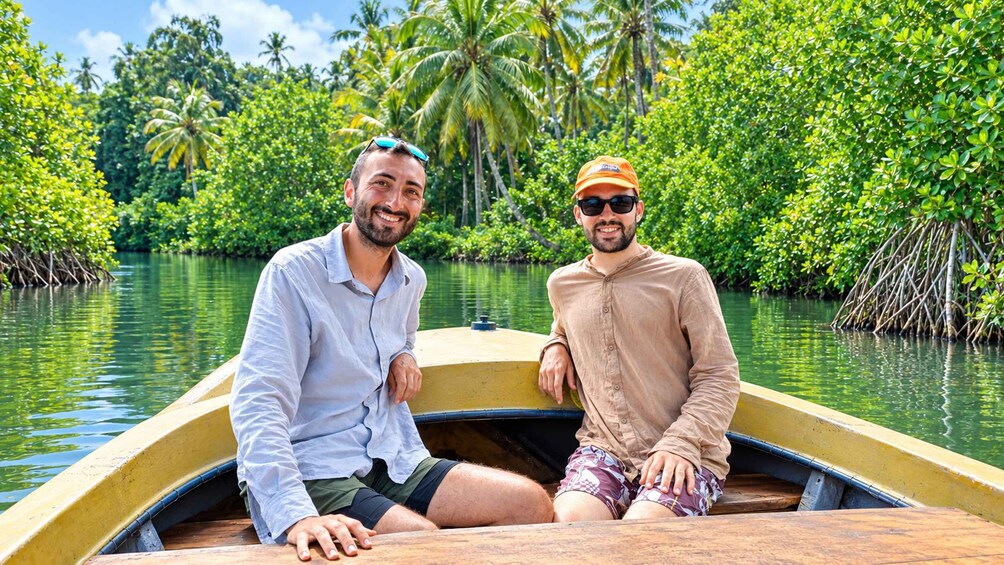 Two people in a boat on a river surrounded by dense greenery and palm trees. 1
