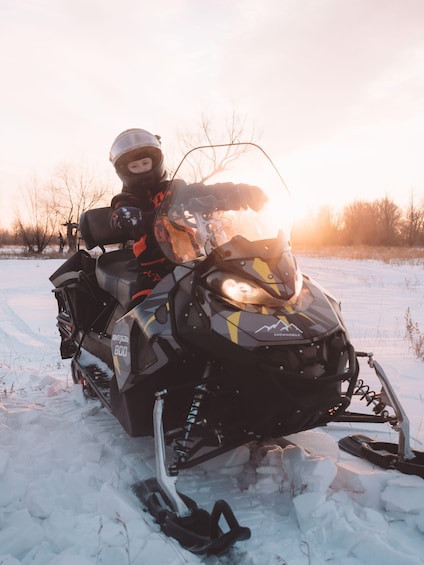A snowmobile with a rider, snow-covered ground, and trees in the background. 2