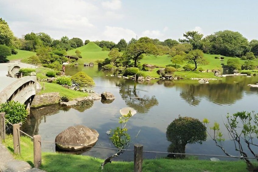 A serene pond with a stone bridge, surrounded by lush greenery and trees. 1
