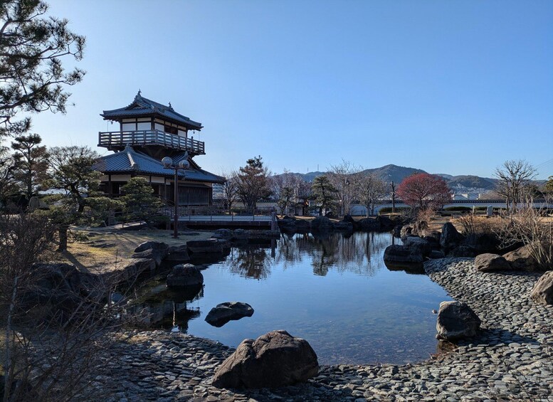 A traditional Japanese building with a tiled roof, surrounded by a calm pond with rocks, and a mountainous backdrop. 2