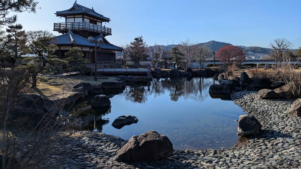 A traditional Japanese pagoda, a calm pond with rocks, and a mountainous backdrop. 2