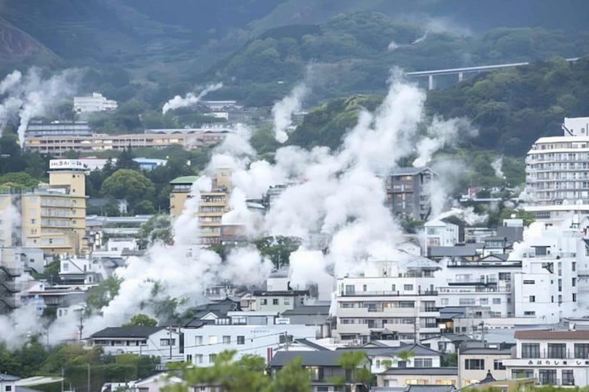 A cityscape with multiple buildings, some emitting smoke, and a mountainous backdrop. 1