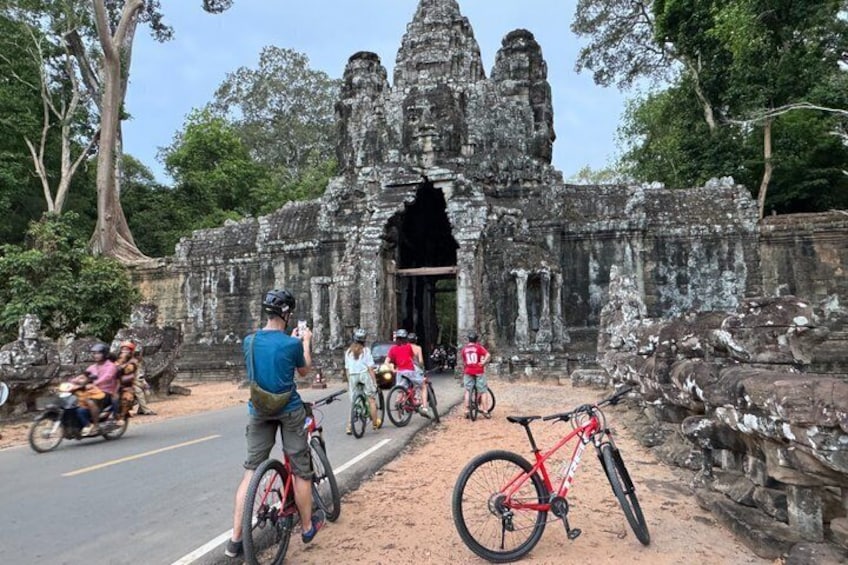 A temple entrance with a red bicycle leaning against it, surrounded by trees and a road with motorbikes. 5