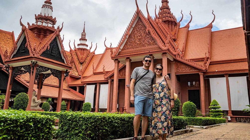 A couple standing in front of a traditional Thai temple with ornate architecture and a well-maintained garden. 3