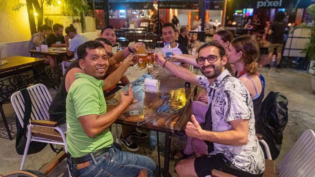A group of people toasting with beer at a table in a casual outdoor setting. 2