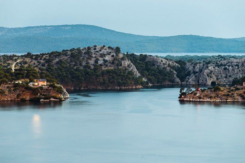 A calm lake surrounded by rocky hills with a few buildings on the shore. 1