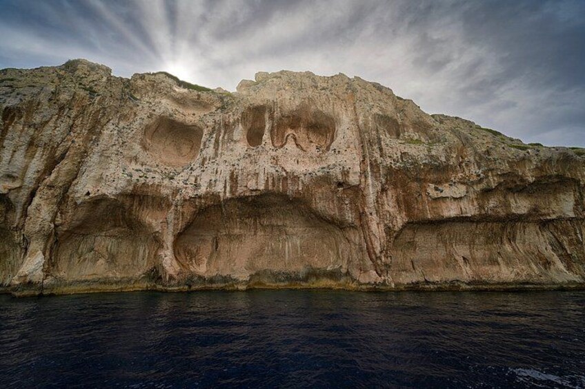 A large rock formation with multiple caves and a body of water in the foreground. 2