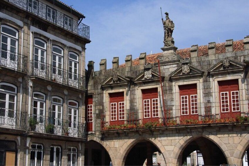 A historic building with red doors, a statue on the roof, and stone arches. 3