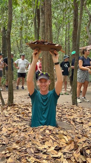 A person holding a wooden board above their head in a forested area with fallen leaves on the ground. 2