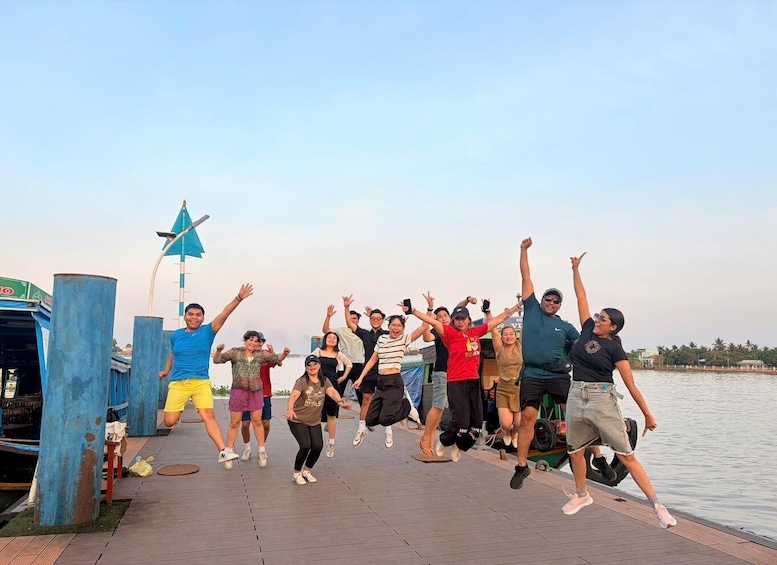 A group of people jumping on a wooden dock by a body of water. 5
