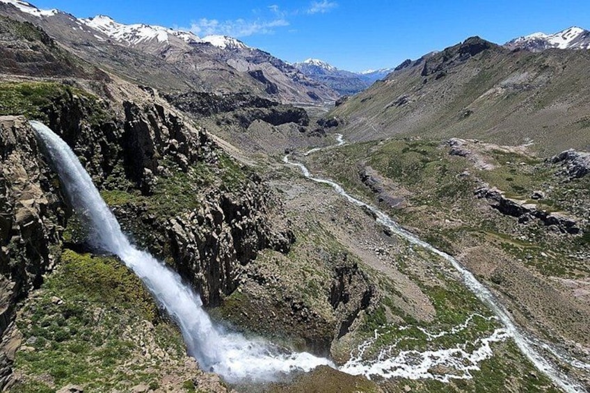 A waterfall cascading down a rocky cliff, surrounded by a mountainous landscape with a river flowing through the valley. 1