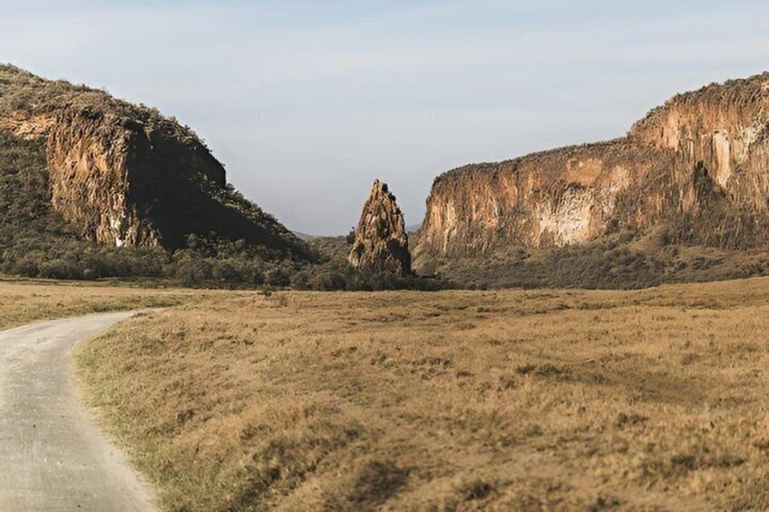 A dirt road curving through a flat landscape with rocky cliffs on either side. 4
