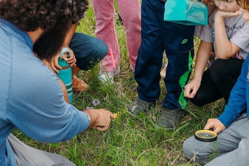 A group of people outdoors, some sitting and some standing, engaged in an activity with a water bottle and a compass. 5