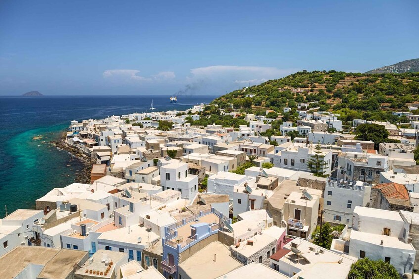 A coastal town with white buildings, a clear blue sea, and a hilly landscape in the background. 2