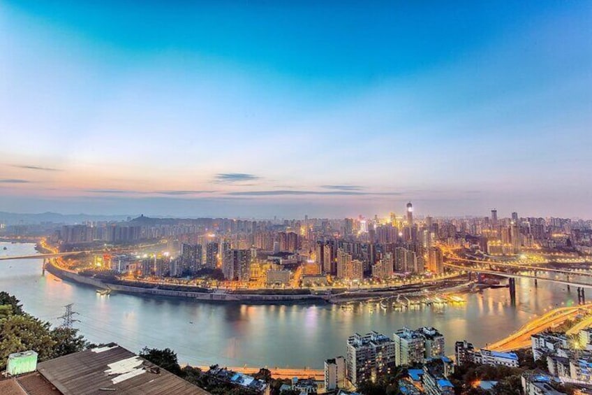 En bysilhouet i skumringen med oplyste bygninger, en flod og en bro. 3