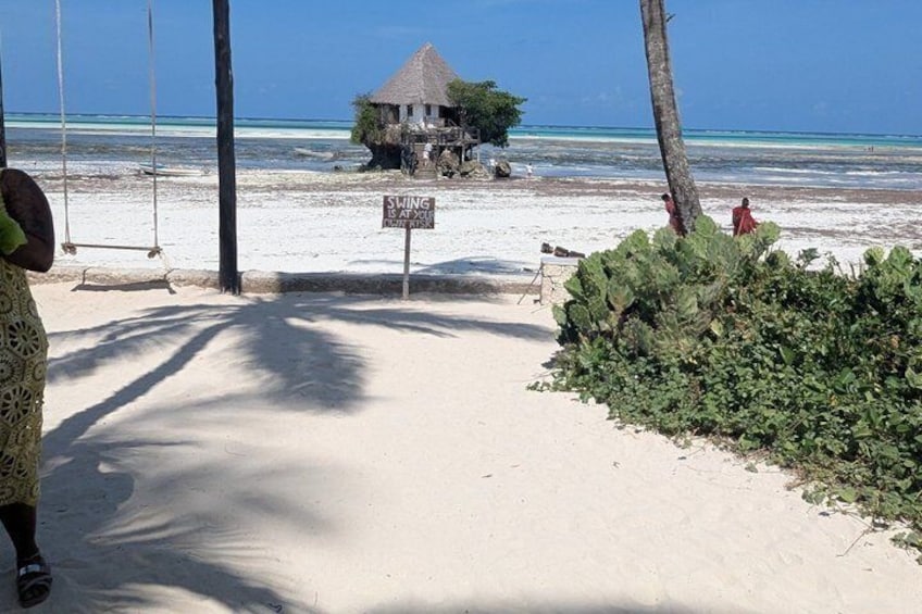 Una playa con un columpio, una cabaña de techo de paja y un cartel que indica zona de columpios. 1