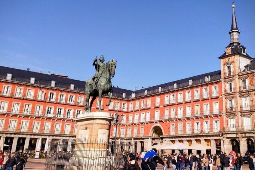 A historic building with a statue of a figure on horseback, a church spire, and a crowd of people. 2
