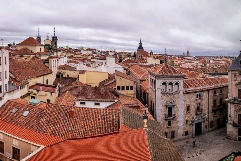A cityscape with red-tiled rooftops, historic buildings, and a cloudy sky. 4