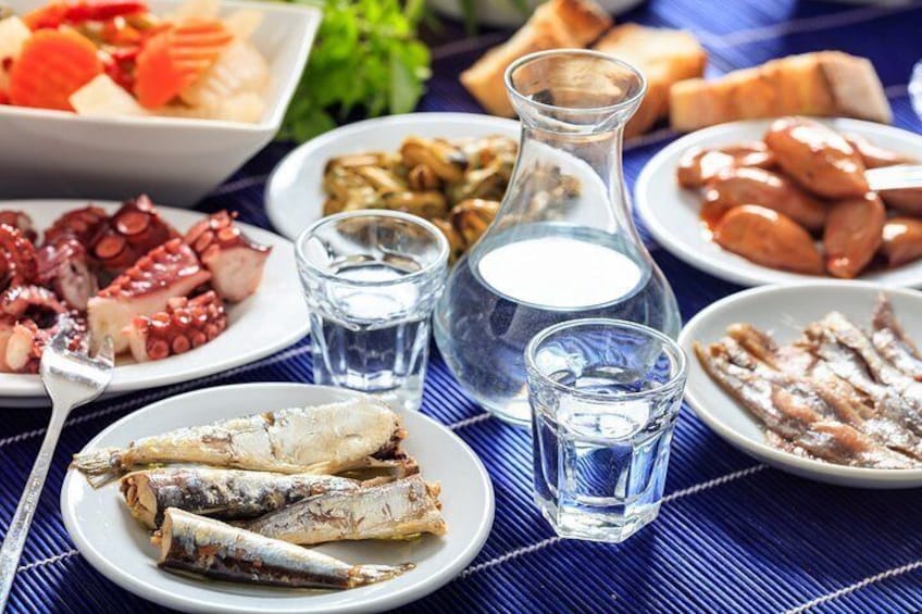 A table with various seafood dishes, including octopus, fish, and sausages, along with glasses of water. 4