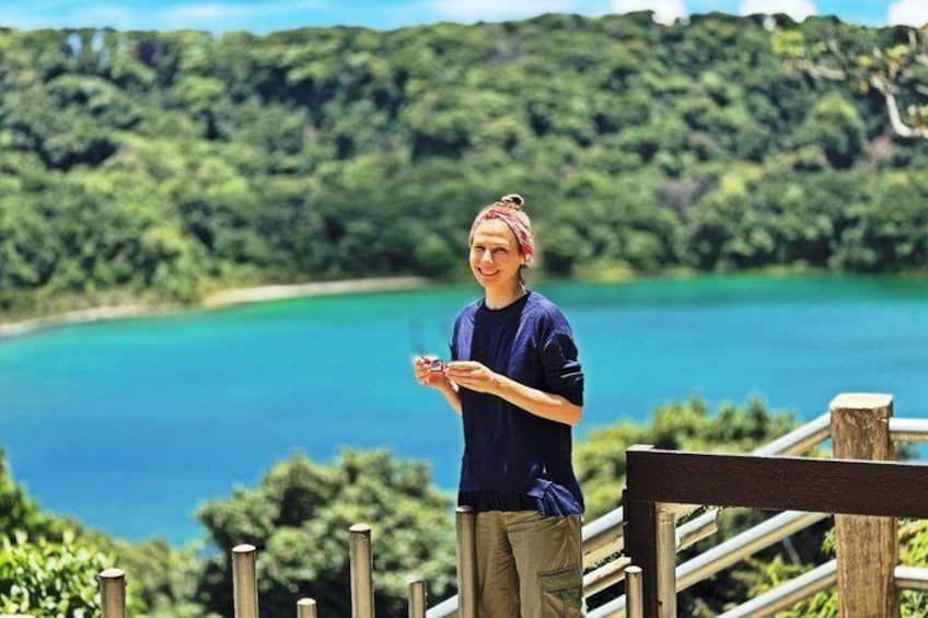 A person standing on a wooden deck overlooking a turquoise lake with dense greenery in the background. 1