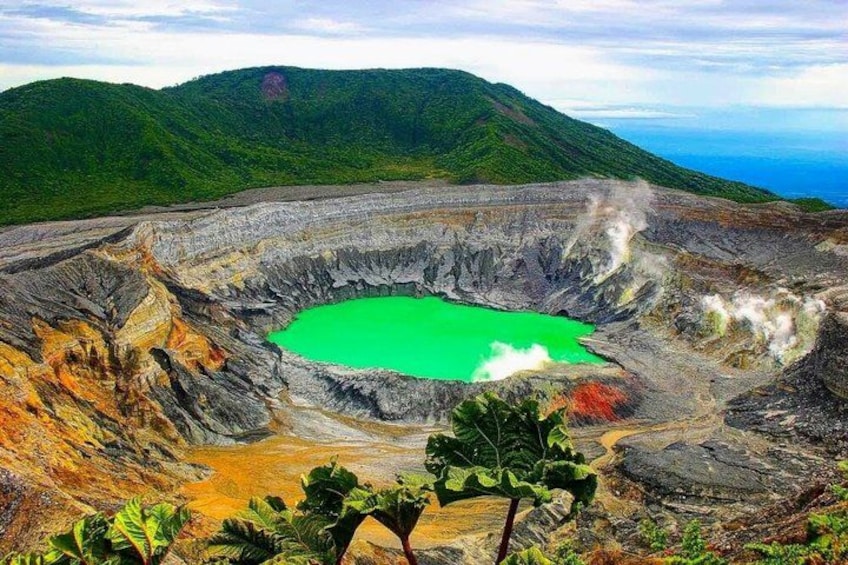 Ein großer Krater mit einem grünen See, umgeben von zerklüftetem Gelände und Bergen. 2