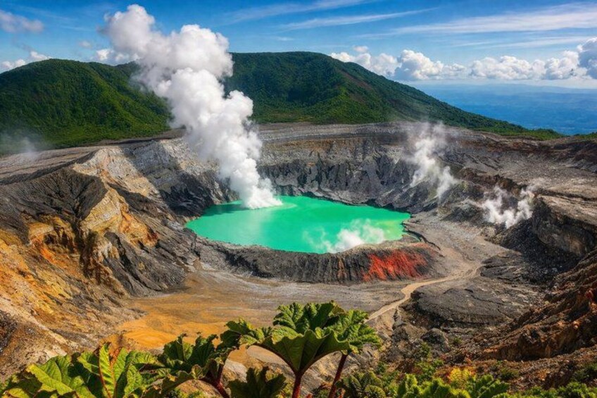 Ein Vulkankrater mit einem türkisfarbenen See, Dampfaustritten und umgebender Vegetation. 1