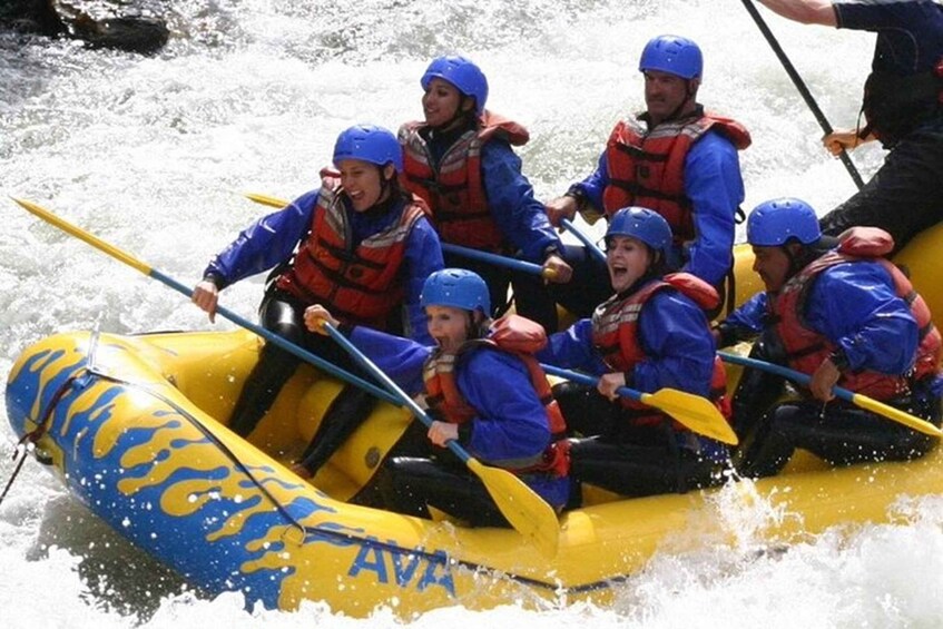 A group of people in a yellow inflatable raft with blue flames design, paddling through a river. 1
