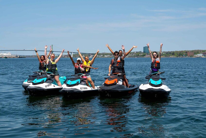 People on jet skis with arms raised, water in the foreground, and a bridge in the background. 5