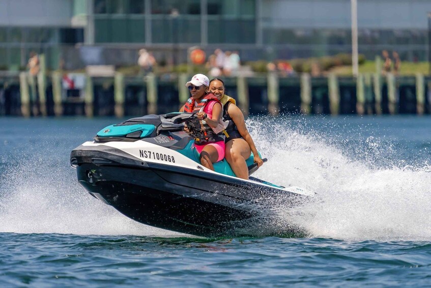 A jet ski with two people wearing life jackets, moving through water, with a dock and people in the background. 1
