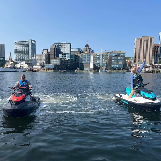 Two people on jet skis in a body of water with a city skyline in the background. 3