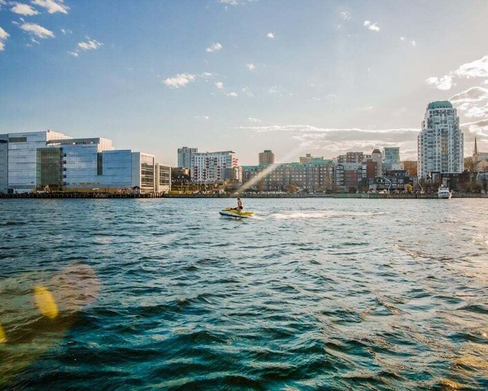 A city skyline across a body of water with a person on a jet ski. 2