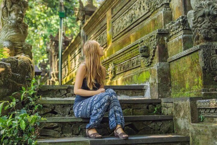 A person sitting on stone steps with intricate carvings and statues in a lush, green environment. 5