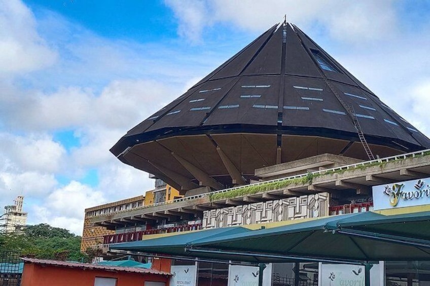 Una estructura arquitectónica moderna con un techo distintivo en forma de pirámide, rodeada de edificios comerciales y un cielo despejado. 4