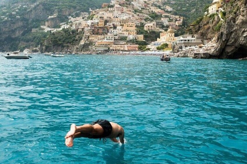 A person swimming in clear blue water with a coastal town in the background. 4