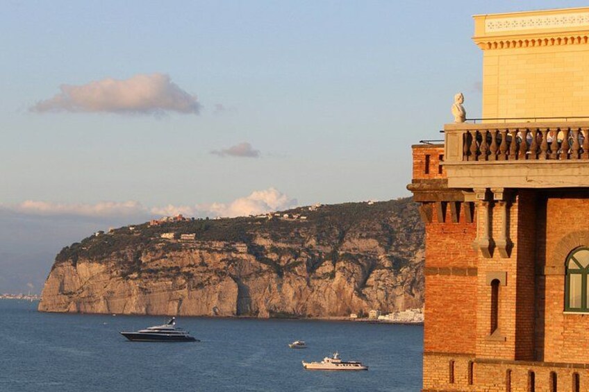 A coastal building with a balcony, a rocky cliff, and boats on the water. 5